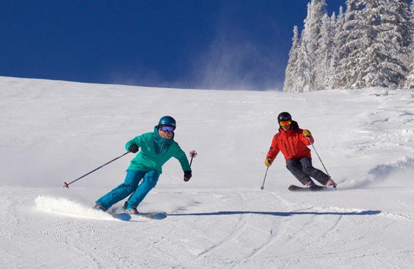 Couple skiing close togehter down a groomed trail.