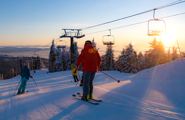 Father and his kids skiing on the mountain at sunset.